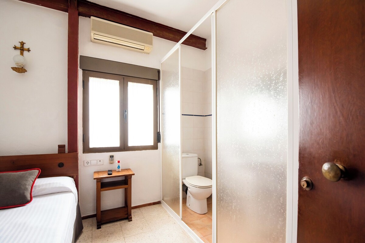 Un dormitorio con cama, mesita de noche, ventana, inodoro y zona de ducha.