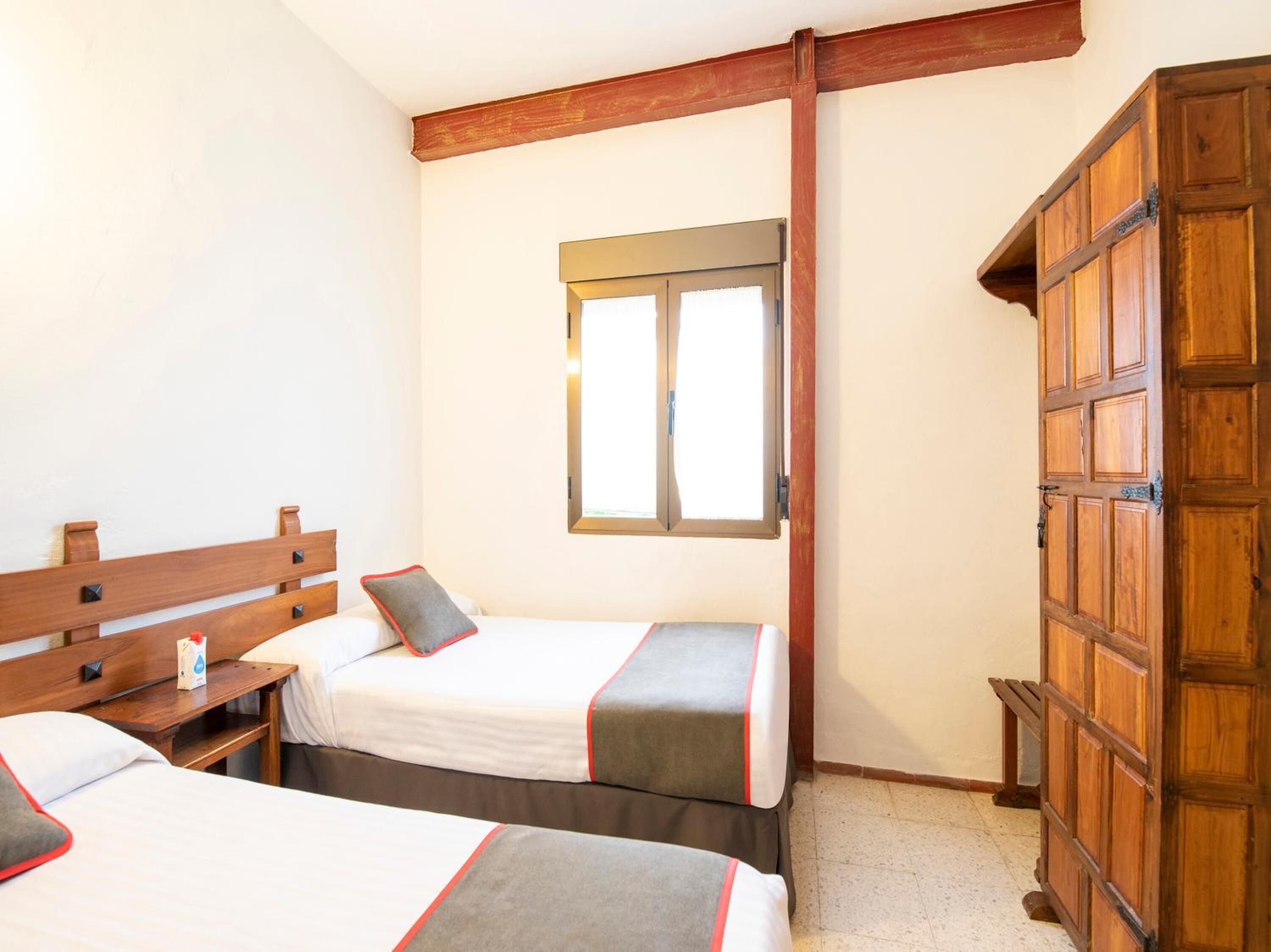 Una habitación de hotel con dos camas, un armario de madera, una ventana y una viga de madera en el techo.