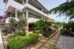 A modern building with a covered outdoor area, potted plants, and a stone pathway. - Pool & Garden Apartment Bakija (Pakostane)