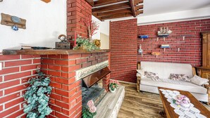 A living room with a brick fireplace, a white sofa, and a wooden coffee table. - Pool & Garden Apartment Bakija (Pakostane)