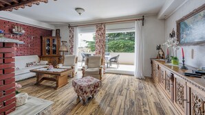 A spacious living room with a wooden floor, a brick accent wall, a sofa, a coffee table, and a balcony with a view. - Pool & Garden Apartment Bakija (Pakostane)