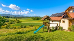 Een huis met een speelhuisje met rieten dak, een blauwe glijbaan en zonnepanelen.