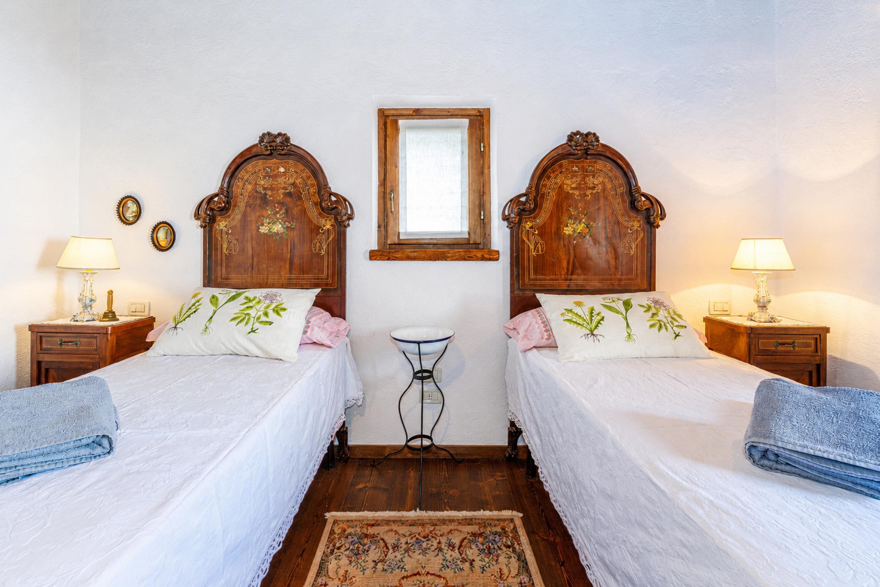 A double room with two beds, wooden headboards, bedside tables with lamps, a small round table, and a window.