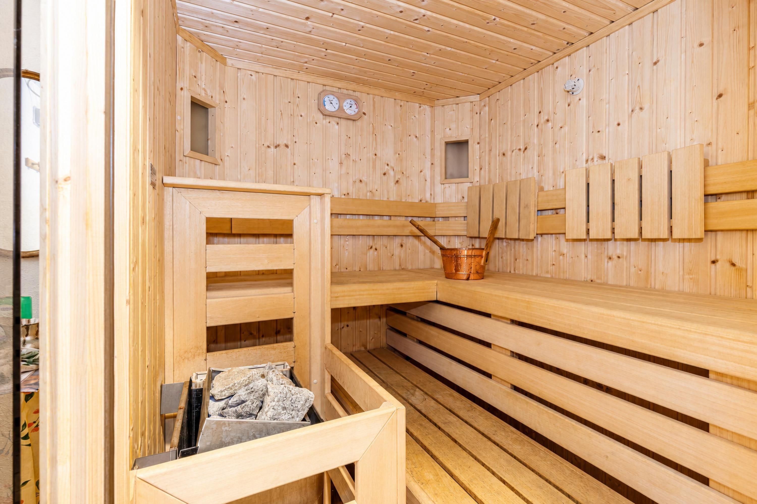 Eine Holzsauna mit Bänken, einem kleinen Fenster und einem Kupferkübel.