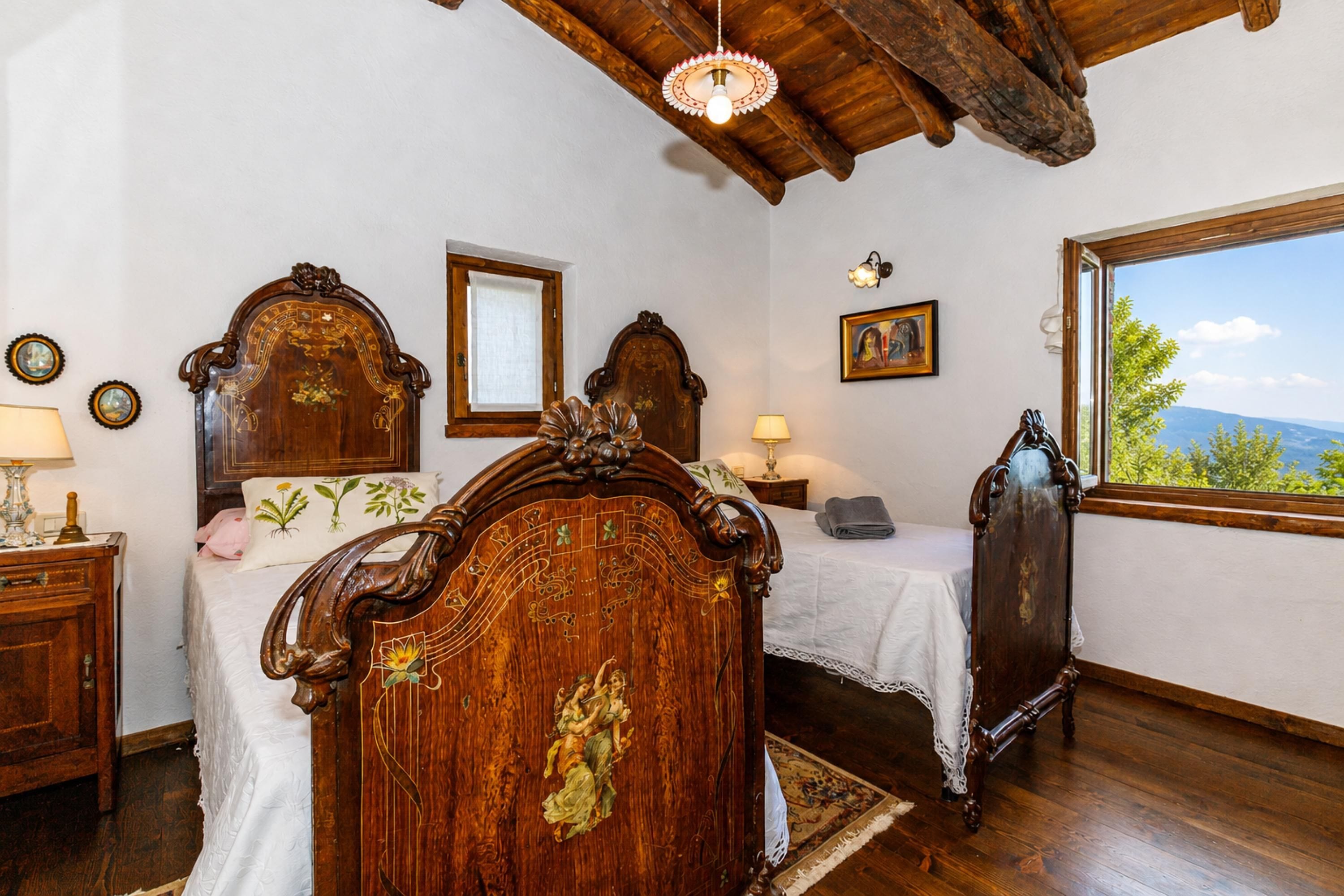 A bedroom with a wooden bed, a nightstand, a dresser, a window with a view, and a chandelier.