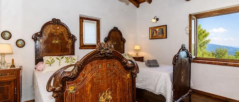 A bedroom with a wooden bed, a nightstand, a dresser, a window with a view, and a chandelier.