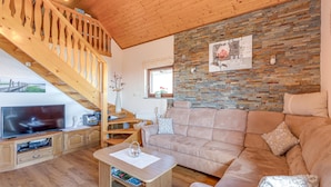 A cozy living room with a wooden staircase, a flat-screen TV, a beige sofa, and a brick-patterned wall. - Vineyard Cottage Bahor (Crnomelj)