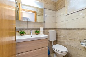 A bathroom with a wooden vanity, a white sink, two potted plants, a toilet, and a mirror.