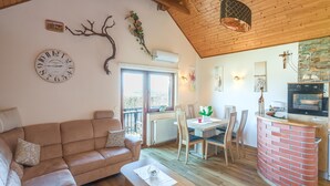 A cozy living room with a wooden ceiling, a brown sofa, a dining table with chairs, and a kitchen area with a brick counter. - Vineyard Cottage Bahor (Crnomelj)