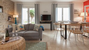 Ein Wohnzimmer mit grauem Sofa, einem Esstisch mit Stühlen, einem Fernseher und einer Steinwand.