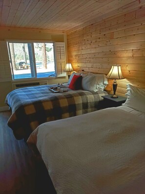 A cozy room with two beds, a window with a view of trees, and a table with a tray of items.
