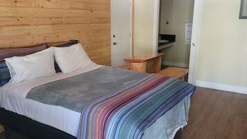 A bedroom with a wooden headboard, a bed with white and gray bedding, a colorful striped blanket, and a small wooden nightstand.