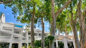 Un immeuble à plusieurs étages, doté de balcons et d’une galerie couverte, entouré d’arbres et de verdure.
