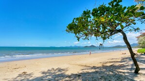 Une plage avec une serviette et un chapeau posés sur le sable, un arbre et l’océan en arrière-plan.