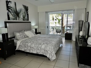 A bedroom with a large bed, nightstands, a dresser, and a balcony with a chair.