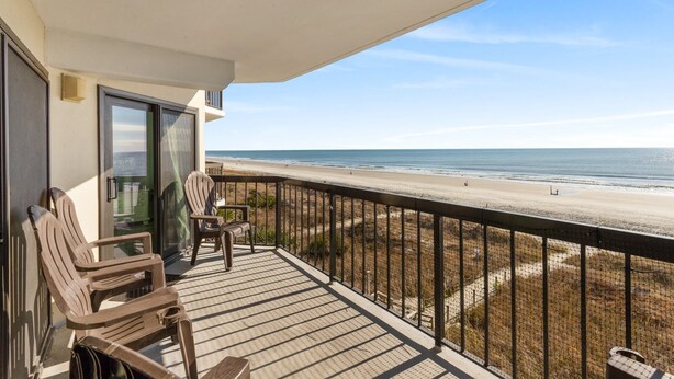 A balcony with two Adirondack chairs, a glass door, and a view of the beach.