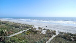 A beach with a clear sky, sandy shore, and a path leading to the water.