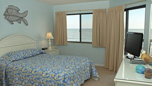 A bedroom with a bed, a desk with a computer, a lamp, and a view of the sea through the window.