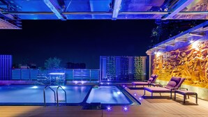 Un espace piscine aménagé sur le toit, avec un mur en pierre et des chaises longues.