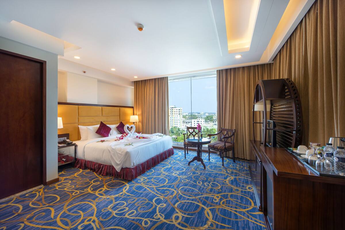 Ein Hotelzimmer mit einem großen Bett, einem Schreibtisch mit Stuhl, Blick auf die Stadt und einem Balkon.