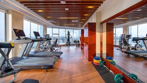 Une salle de sport équipée de tapis de course, d’appareils de musculation et offrant une vue sur la ville.