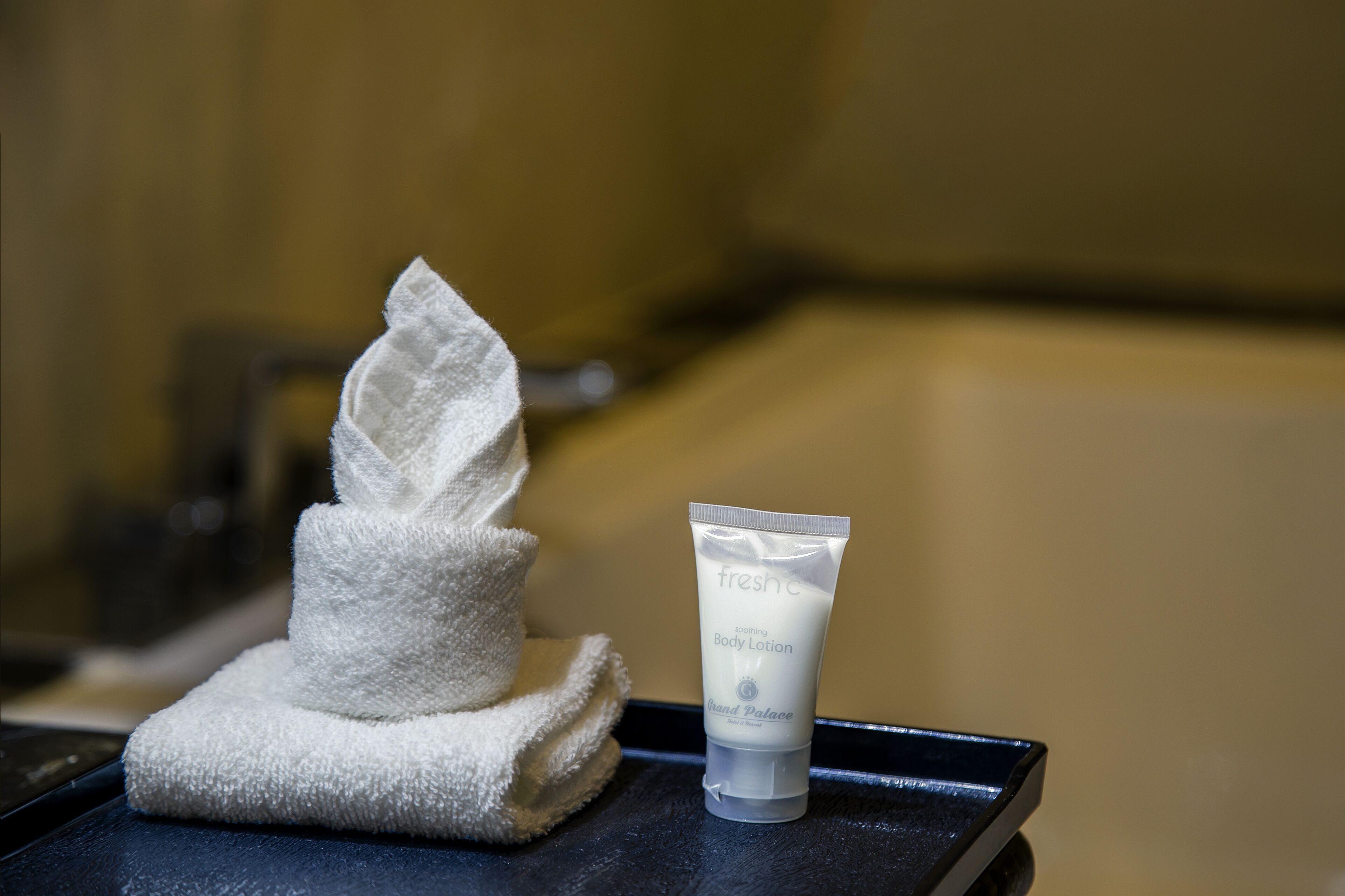A white towel and a tube of fresh body lotion on a black tray.