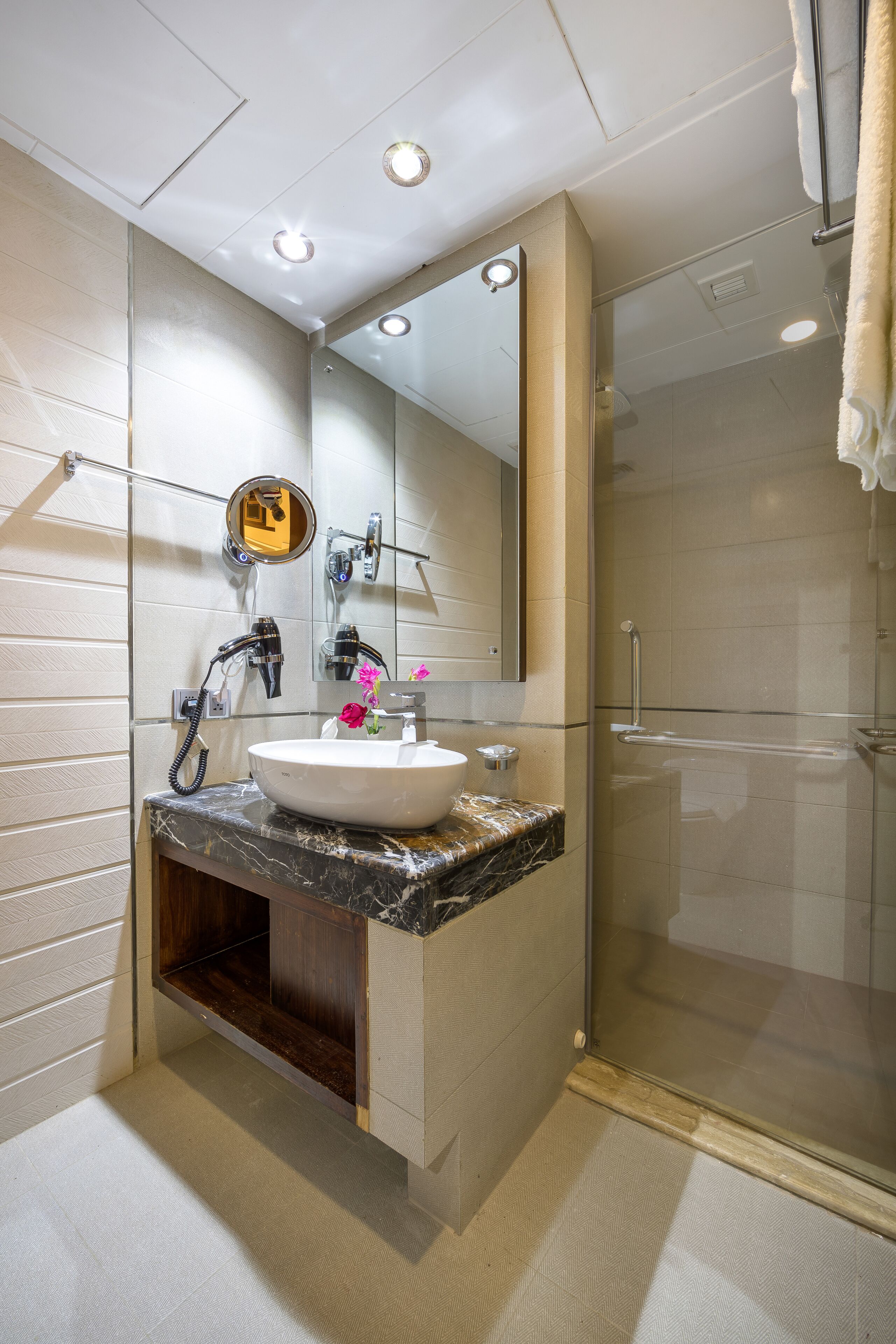 Een moderne badkamer met een grote spiegel, een wastafel met een marmeren blad en een douchecabine van glas.