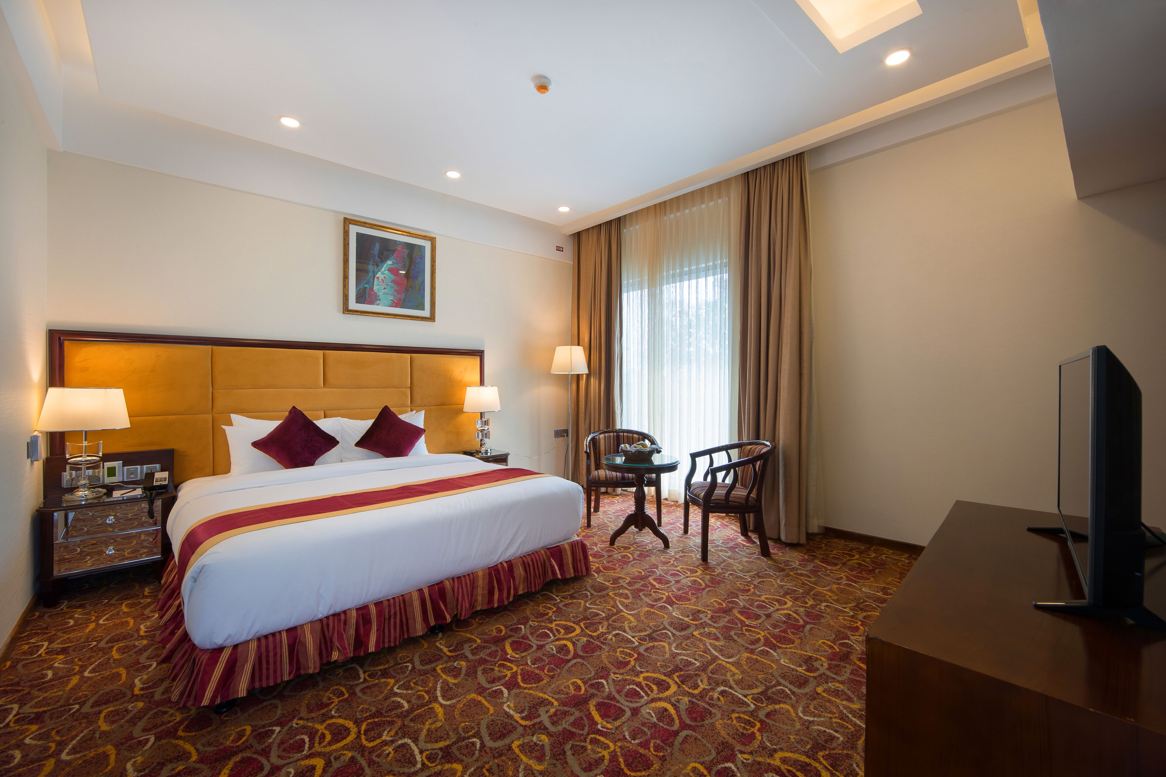 A hotel room with a large bed, two bedside lamps, a desk with a television, and a chair.