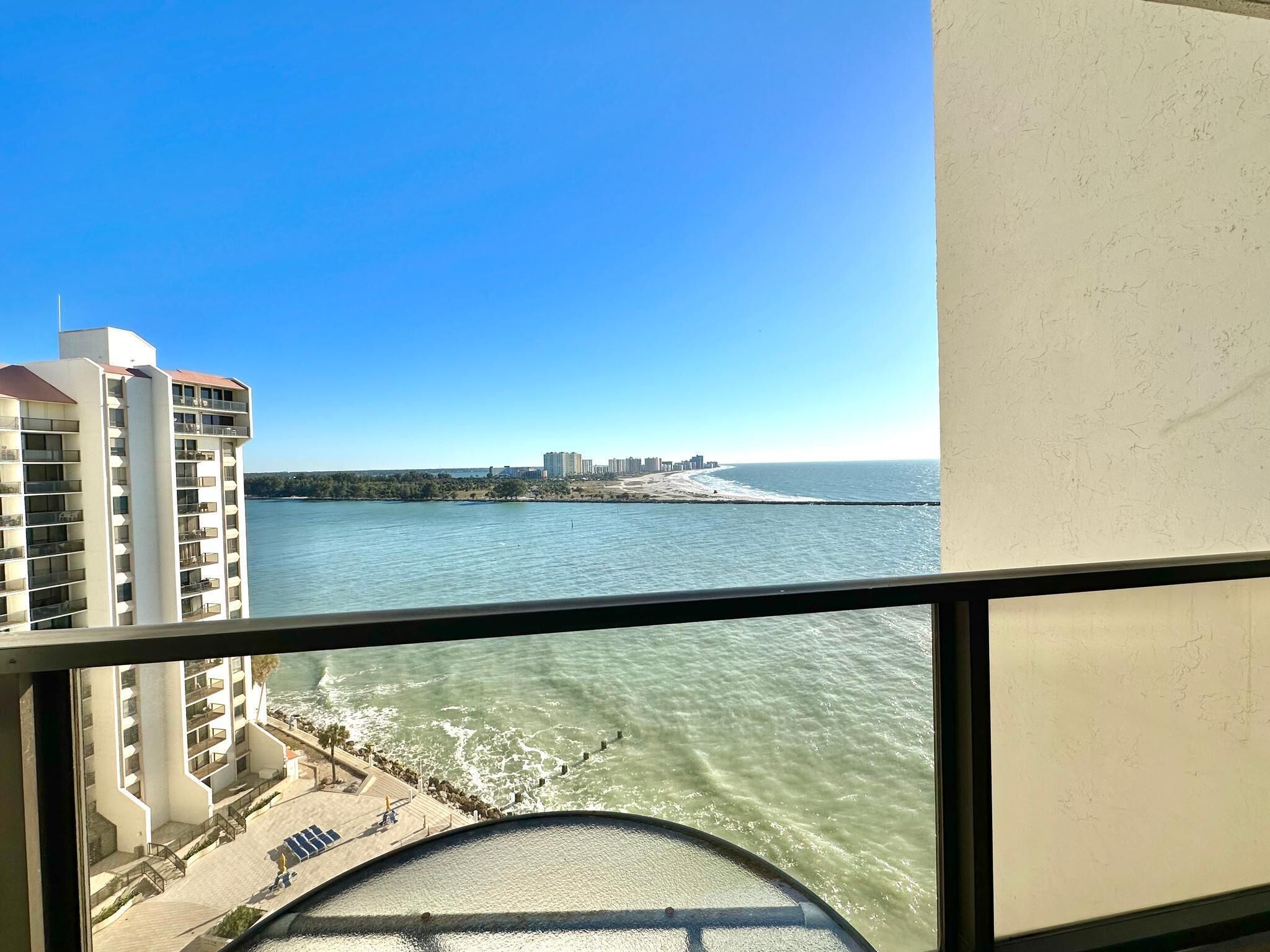 Uitzicht vanaf een balkon op een strand, met een hoog gebouw aan de linkerkant en een uitgestrekte skyline in de verte.