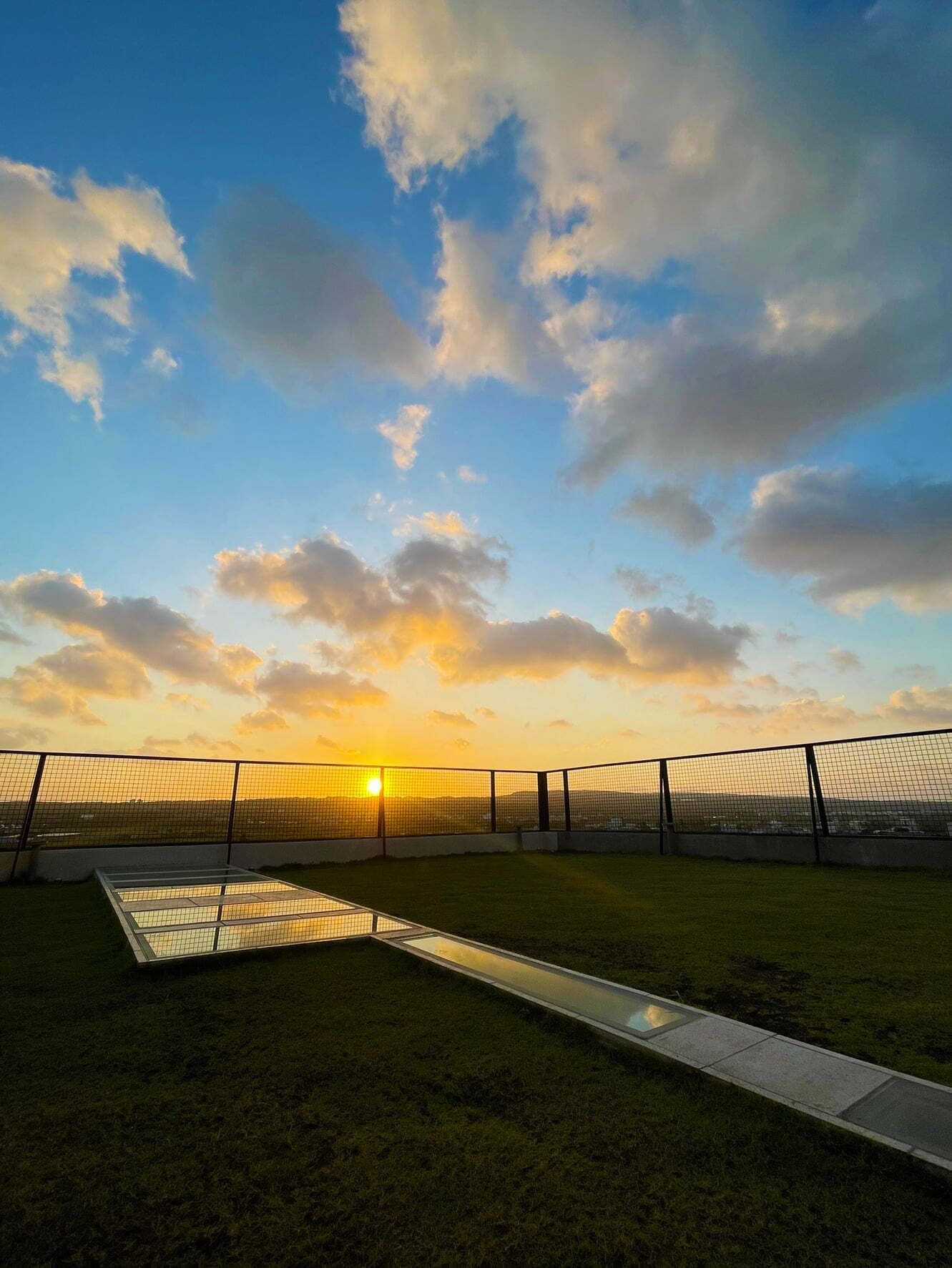 Un espacio al aire libre rodeado por una cerca, con cielo despejado y el sol poniéndose al fondo.