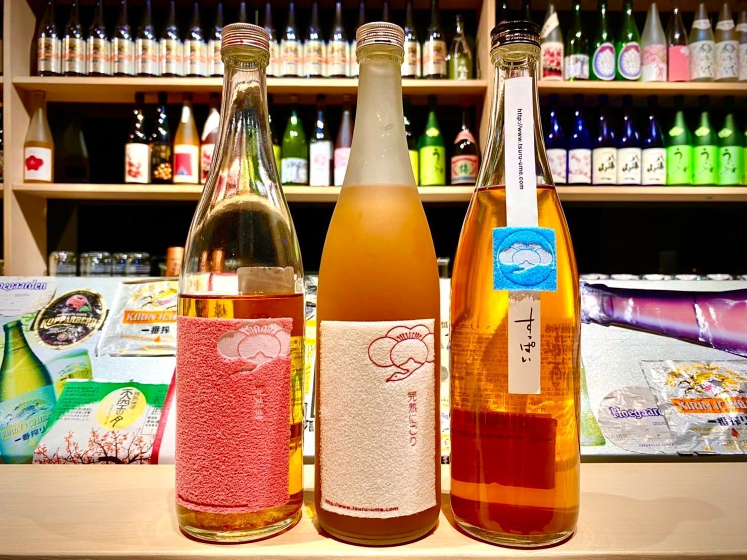 Three bottles with labels on a shelf, surrounded by other bottles.