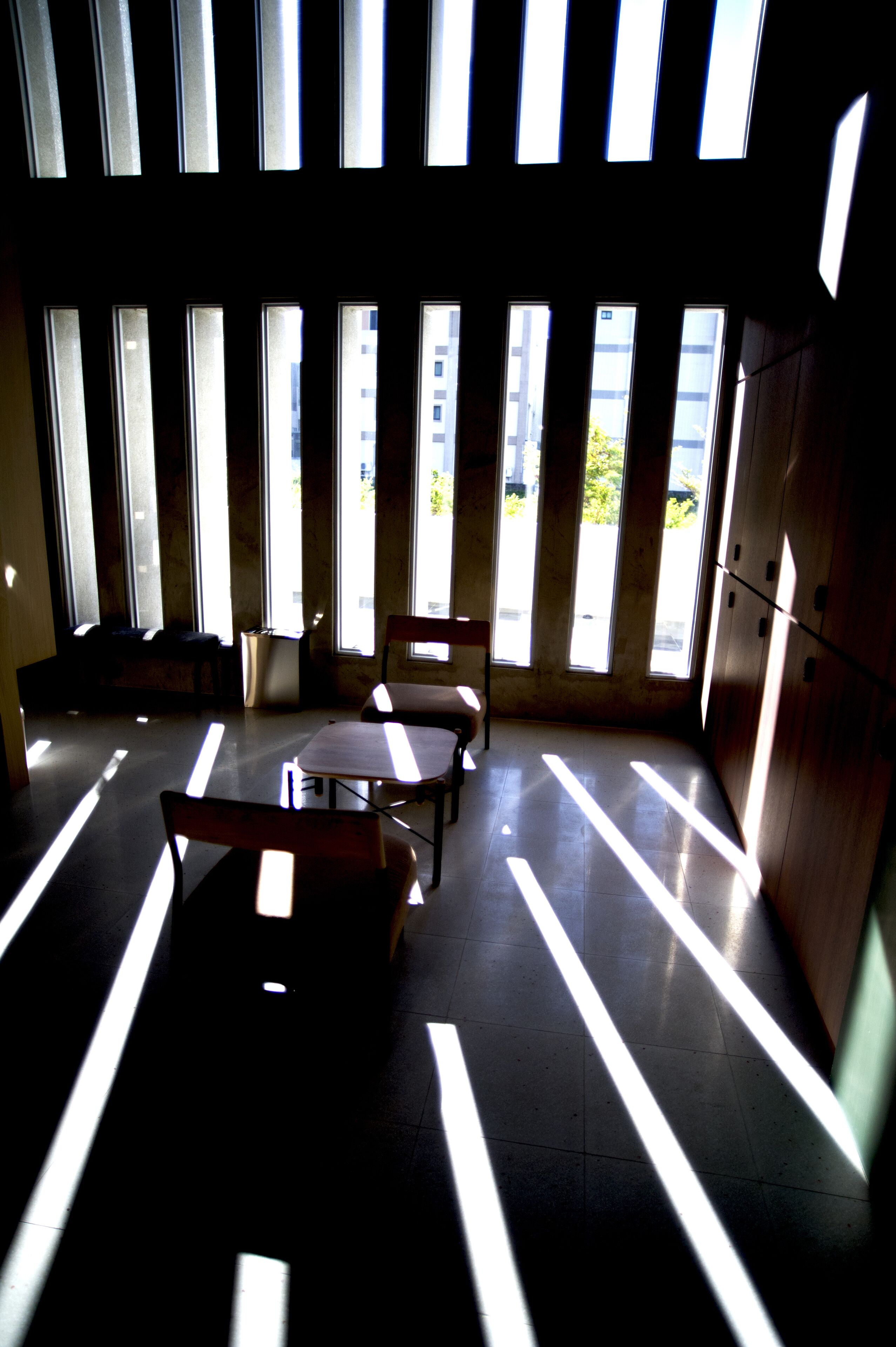 A room with large windows casting shadows on the floor, a table, and chairs.