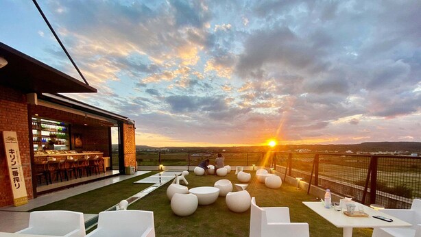 An outdoor seating area with round tables and chairs, a bar with a brick facade, and a sunset view over a landscape. - FFF Hotel (Hengchun)