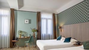 A hotel room with two beds, a desk with a chair, a lamp, and a vase with flowers. - Work From Here at Bristol Hotel (Avignon)