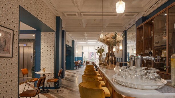 A modern bar area with a long counter, bar stools, and a decorative vase with flowers. - Work From Here at Bristol Hotel (Avignon)