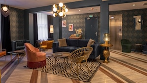 A modern lobby with a blue sofa, a gold chair, and a patterned rug. - Work From Here at Bristol Hotel (Avignon)