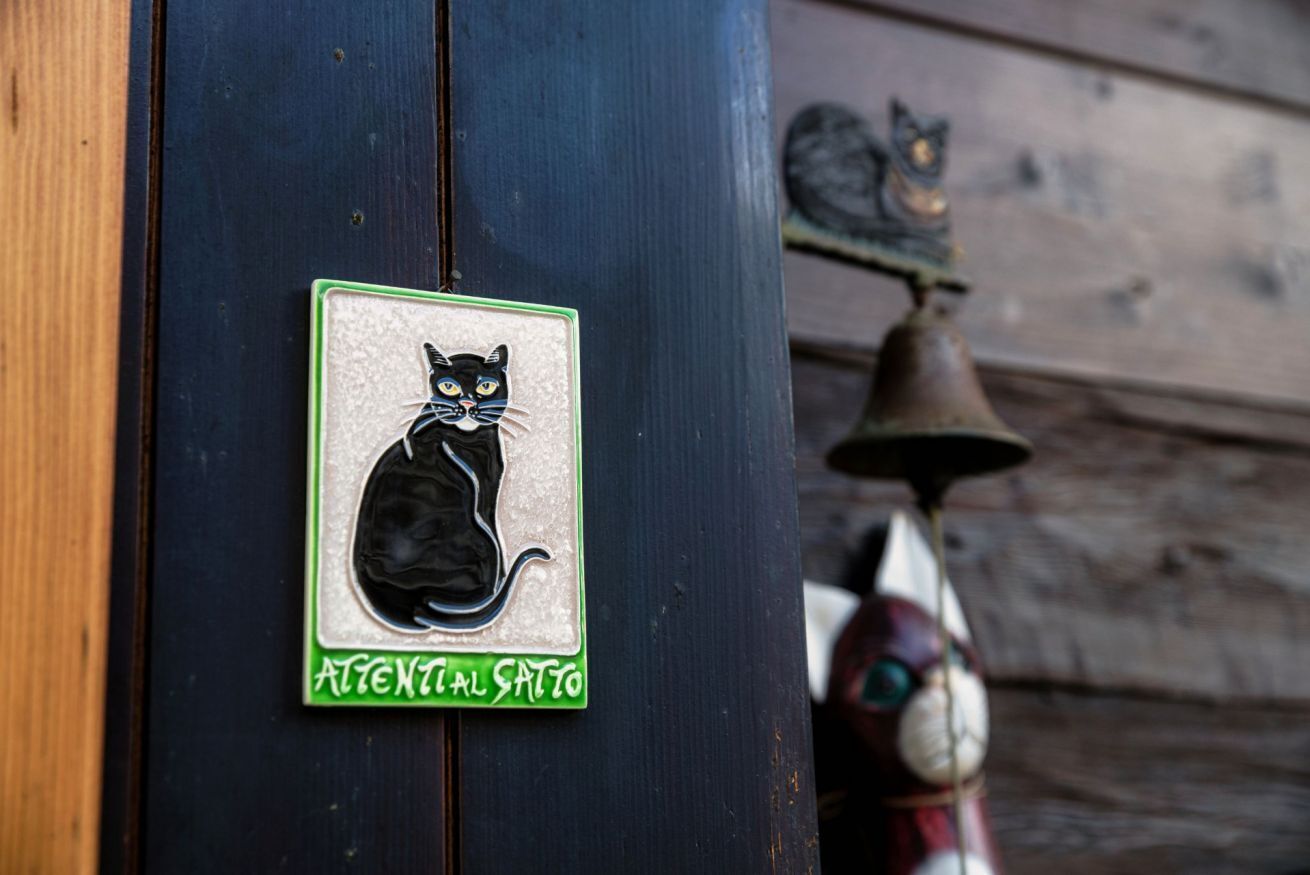 Ein schwarzer Katzenaufkleber an einer Holztür, im Hintergrund eine Türklingel und eine Katzenstatue.