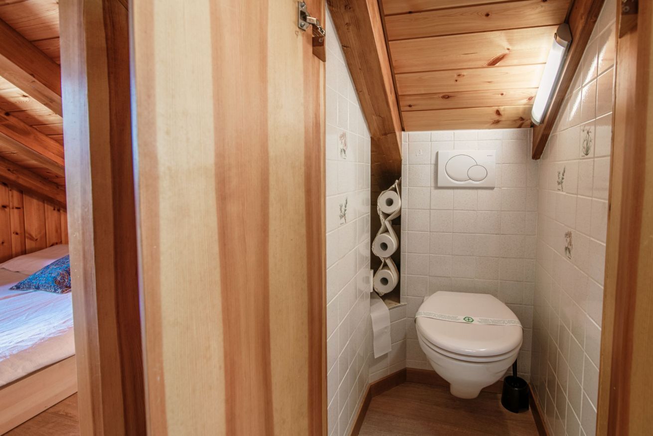 Ein kleines Badezimmer mit Holzvertäfelung, einer Toilette, weißen Fliesen und einer Toilettenpapierrolle an der Wand.