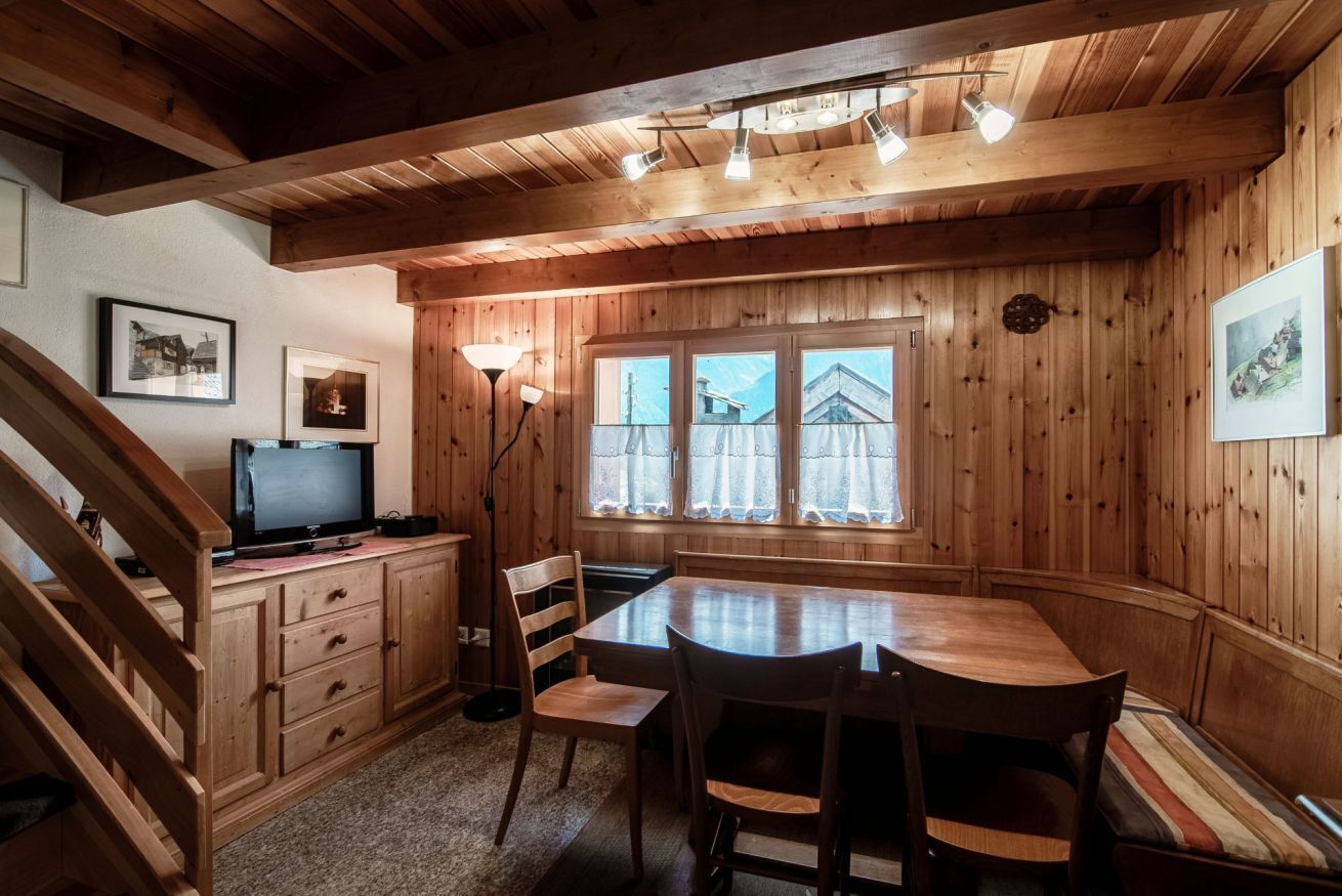 A wooden interior with a dining table, chairs, a television on a cabinet, and framed pictures on the walls.