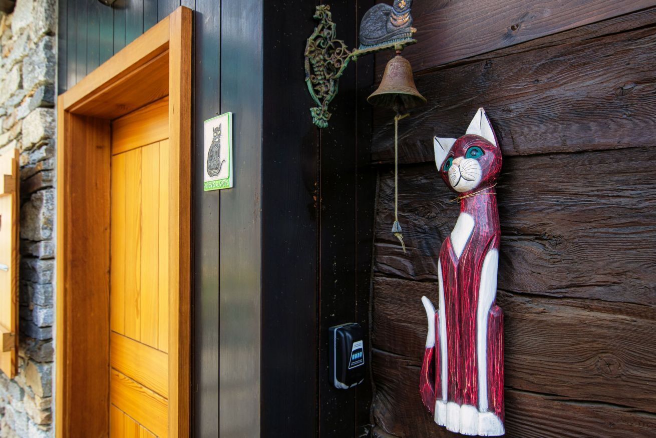 Une porte en bois, avec une cloche et une décoration représentant un chat sur le mur.