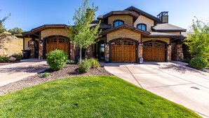 A large, two-story house with a stone facade, multiple garage doors, and a well-maintained lawn. - Luxury Townhome: Hot Tub, Golf, Skiing! Easy Access to Frostwood Gondola (Park City)