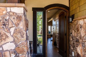 A stone-walled hallway with a wooden door and a view of greenery outside.