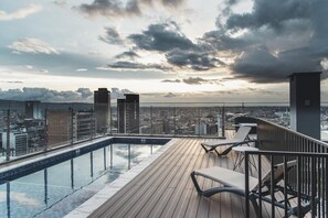 Área de piscina en la azotea con vista a la ciudad, que incluye una piscina y sillas de descanso.
