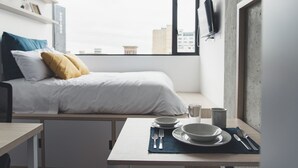 Ein modernes Schlafzimmer mit Bett, Nachttisch und Blick auf die Stadt durch große Fenster.