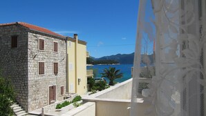 Ein Gebäude aus Stein mit rotem Ziegeldach, daneben ein gelbes Gebäude, im Hintergrund Meer und Berge.