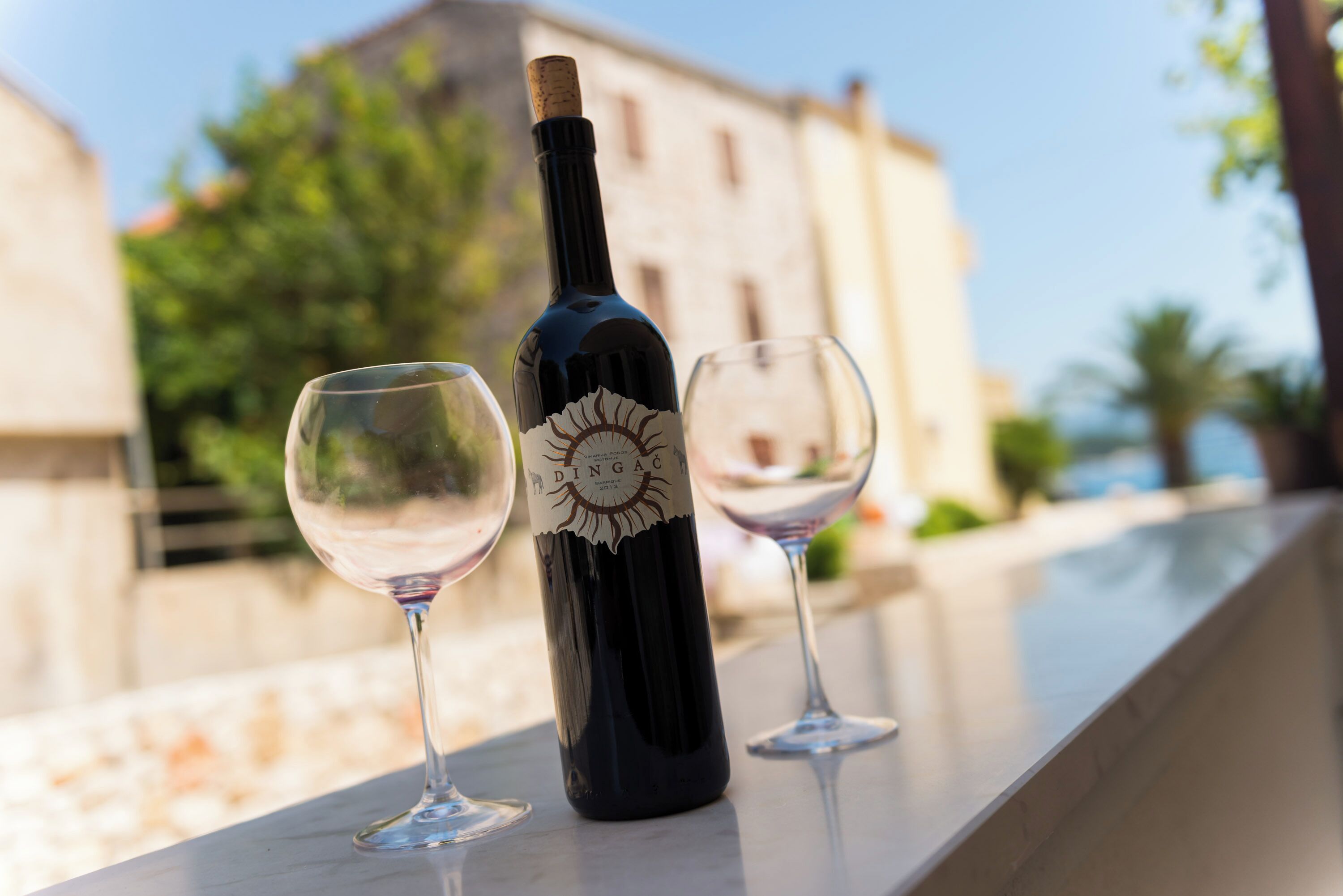 Une bouteille de vin et deux verres sur un balcon, avec un immeuble en arrière-plan.