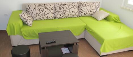 Una sala de estar pequeña y moderna con un sofá verde, una mesita y dos taburetes. Hay un control remoto sobre la mesa.