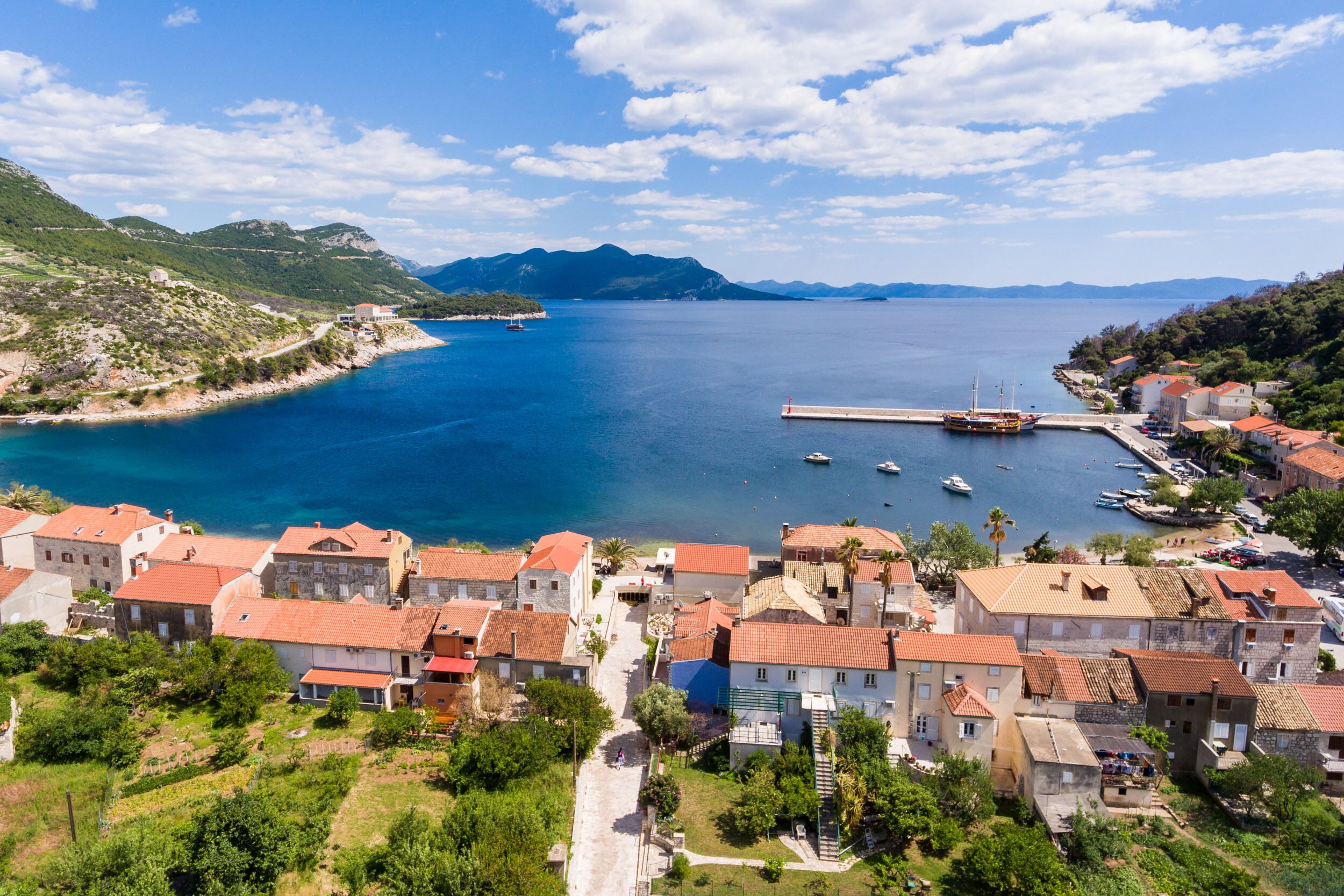 A coastal town with traditional architecture, a marina, and a clear view of the sea and mountains.