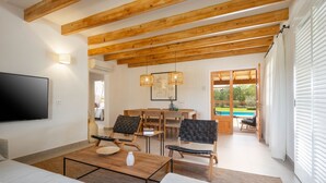 A modern living room with a wooden ceiling, a flat-screen TV, a dining area with a table and chairs, and a view of a swimming pool. - Villa Can Canavaret by SunVillas Mallorca (Pollença)
