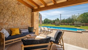 A covered outdoor seating area with stone walls, a pool, and a view of the surrounding landscape. - Villa Can Canavaret by SunVillas Mallorca (Pollença)